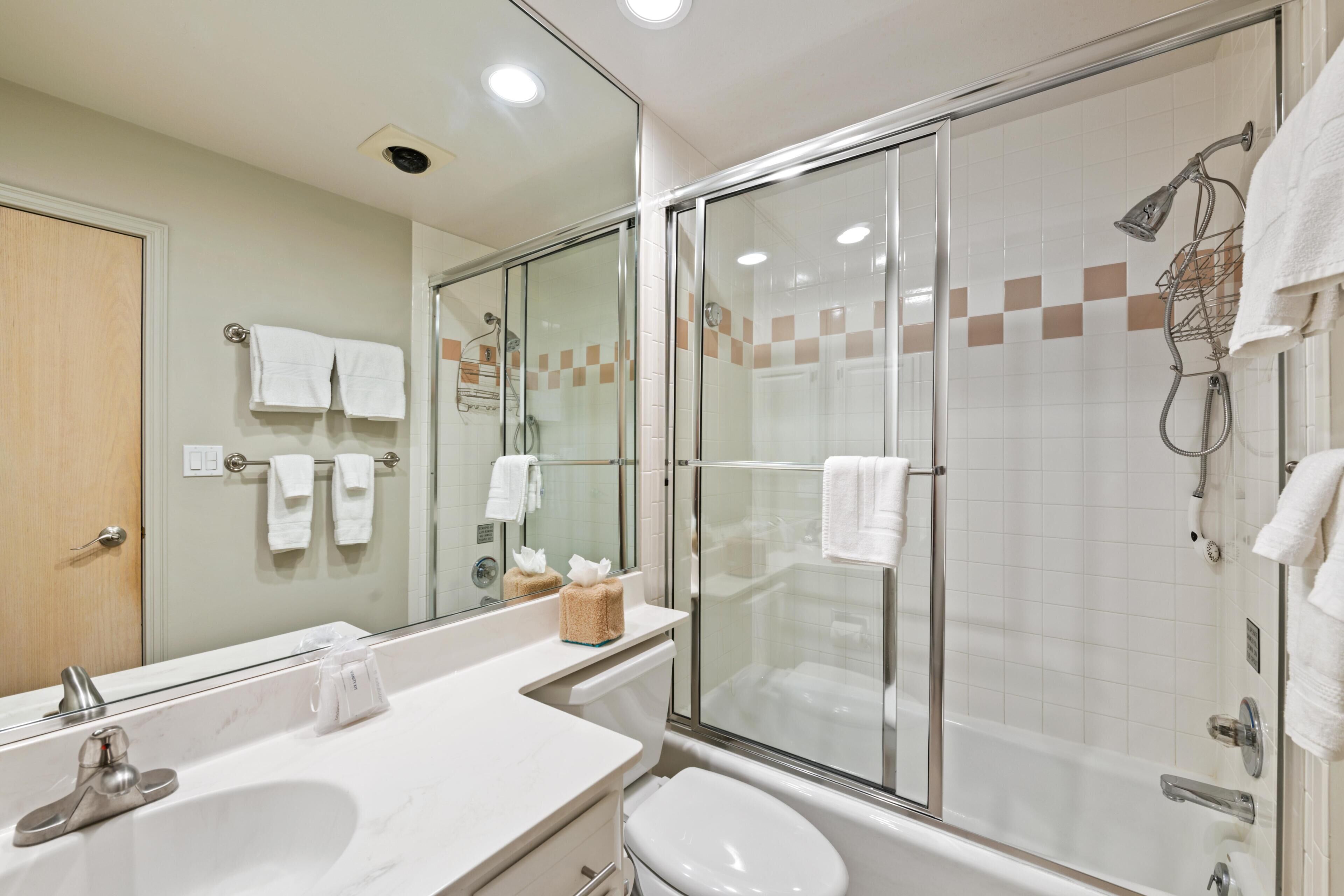 A modern bathroom with a glass-enclosed shower, a large mirror, and a white sink.
