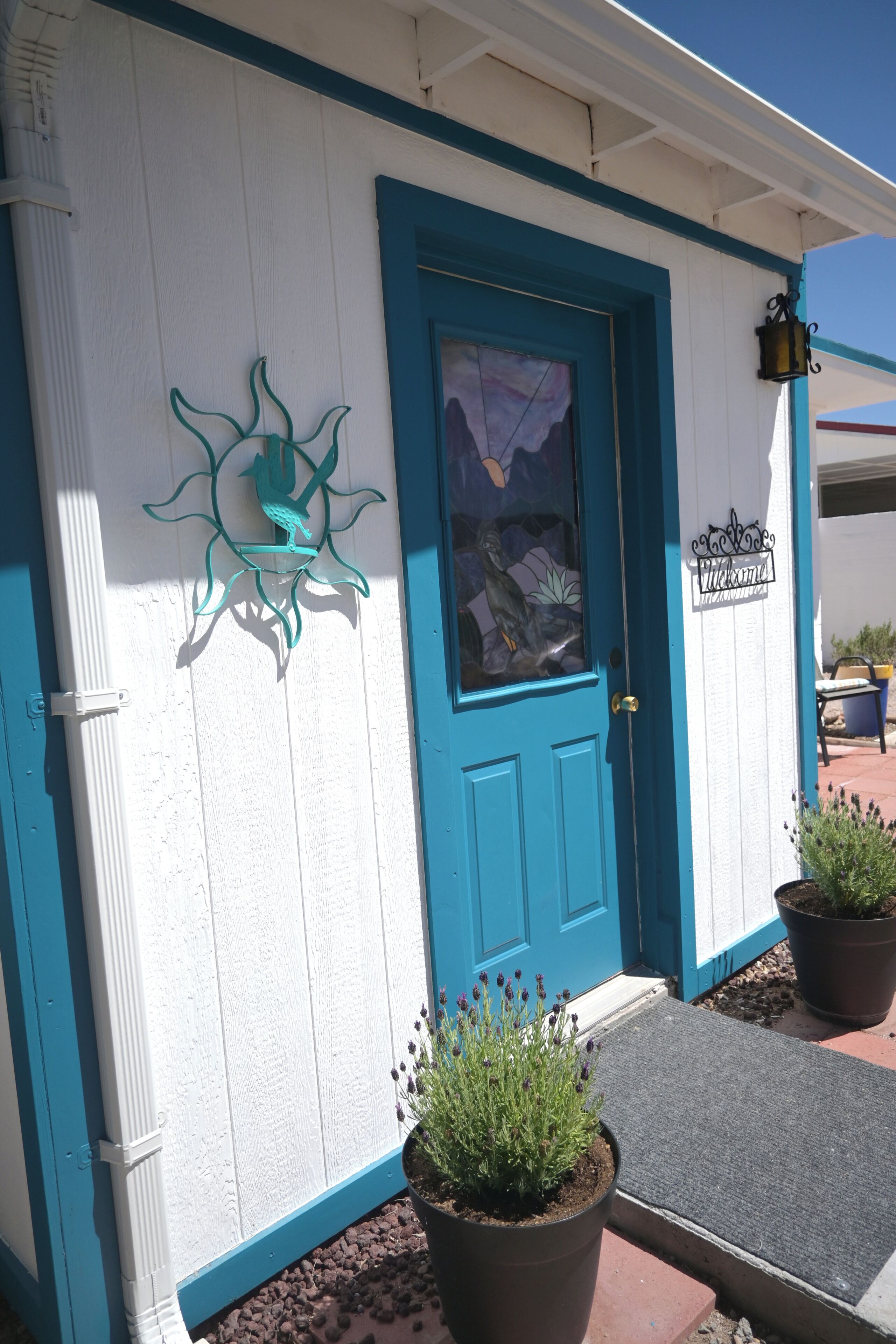 A building with a blue door, a decorative metal piece above the door, and two potted plants in front.