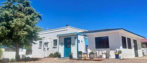 Un edificio blanco con puerta y ventanas azules, rodeado de grava y plantas en macetas.