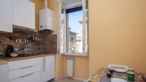 A compact kitchen with a gas stove, a coffee maker, and a window with a view of buildings. - Renovated 2-bedroom apartment in the heart of Pigneto – sleeps 4 (Roma)