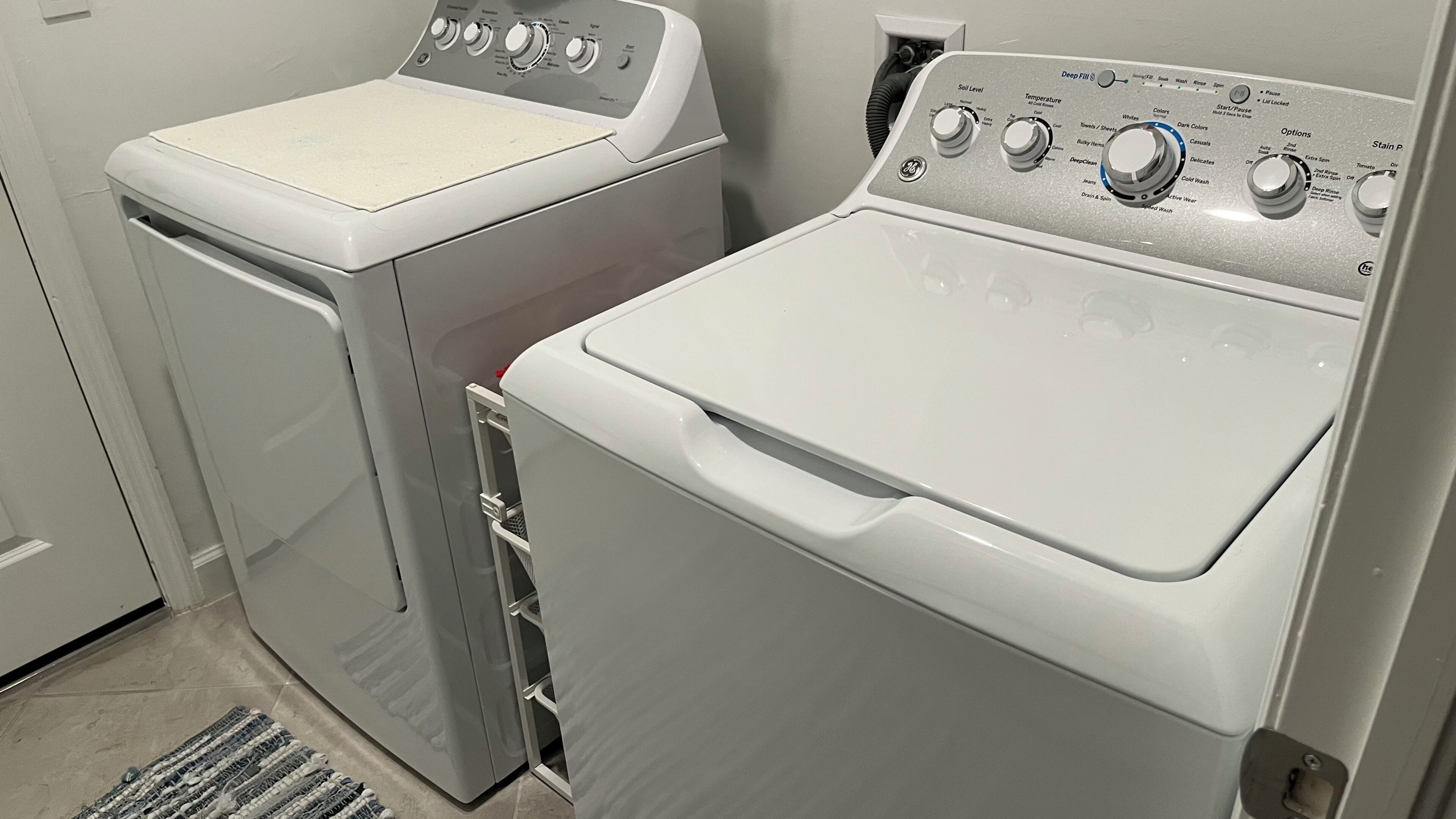A laundry room with two front-loading washing machines, a dryer, and a control panel with various settings.