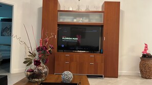 Ein Wohnzimmer mit einer Holz-Unterhaltungsanlage, einer Glasvase mit Blumen und einer dekorativen Kugel auf einem Couchtisch.
