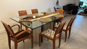 Ein Essbereich mit einem Tisch mit Glasplatte, Holzstühlen, gewebten Unterlagen und einem Blumentopf.
