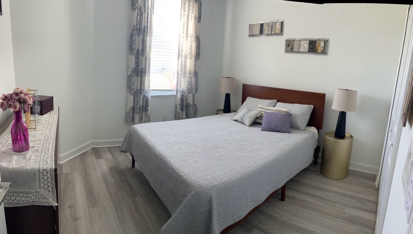 A bedroom with a bed, two bedside lamps, a window with curtains, and wall art.