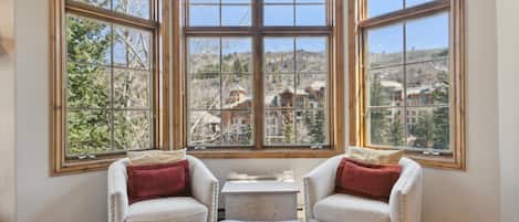 A room with a large bay window, two armchairs, a small table, and a leather ottoman.
