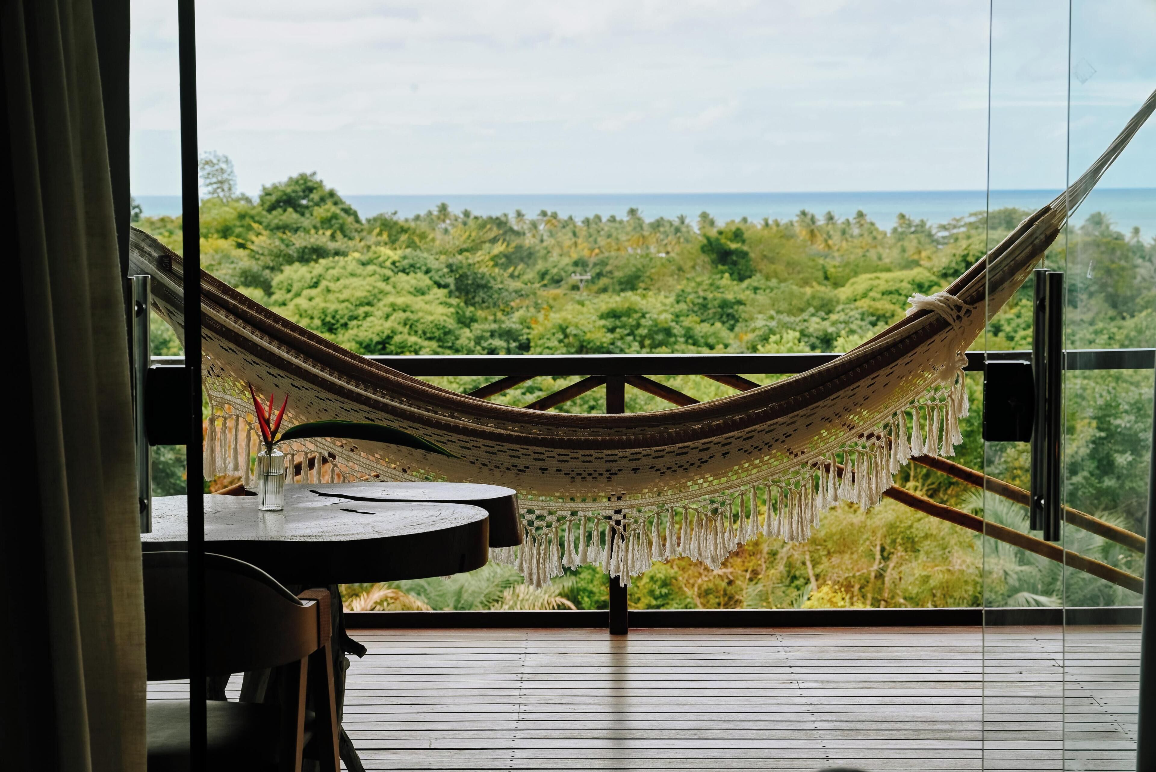 Un hamac sur un balcon donnant sur un paysage boisé, avec vue sur la mer.