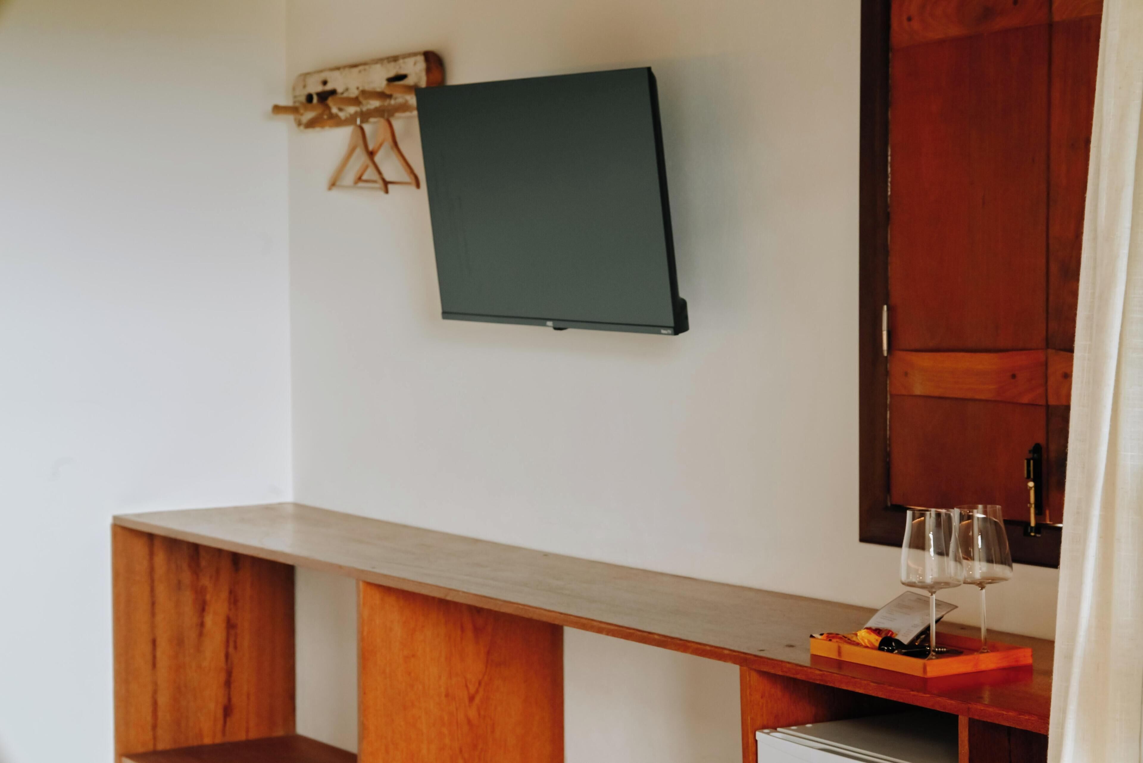 Une pièce avec un bureau en bois, un téléviseur à écran plat fixé au mur et un verre à vin posé sur le bureau.