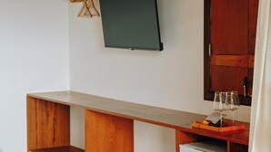 Una habitació amb escriptori de fusta, televisió de pantalla plana penjada a la paret i copa de vi sobre l'escriptori.