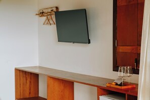Una habitación con un escritorio de madera, un televisor de pantalla plana en la pared y una copa de vino sobre el escritorio.