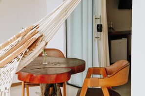 A hammock, a round wooden table, and a wooden chair in a room with a door and a cabinet in the background.