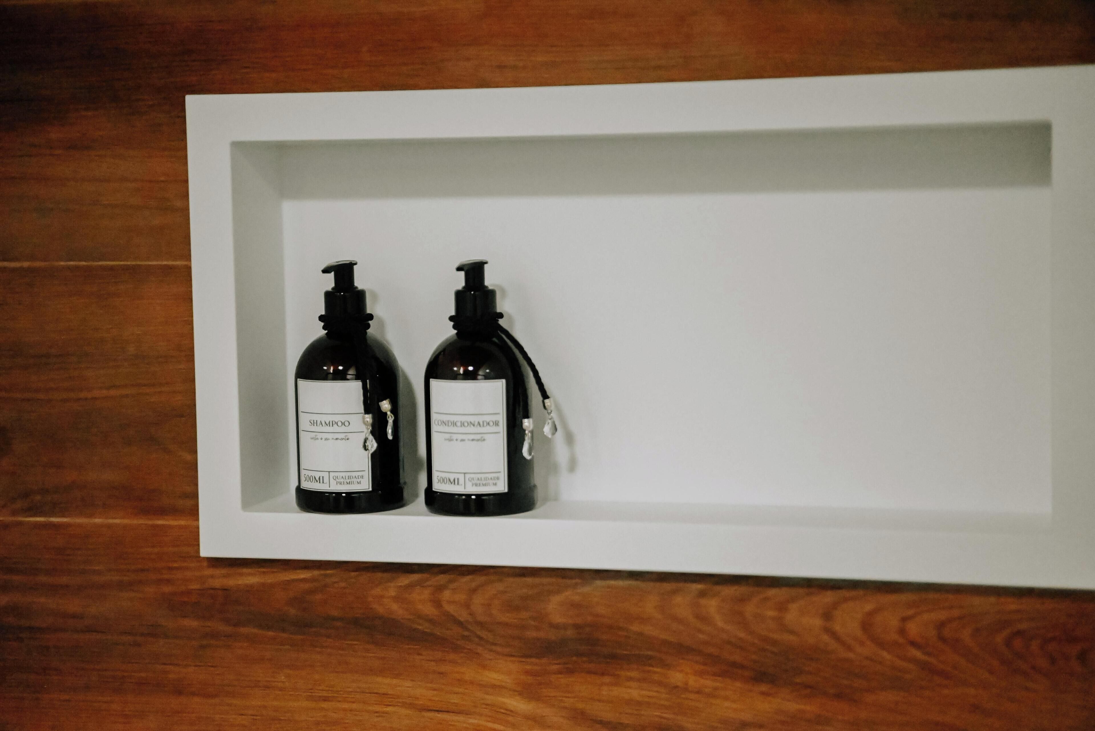Dos botellas negras con dosificadores de bomba en un expositor blanco sobre un suelo de madera.