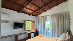 A bedroom with a wooden ceiling, a bed with white bedding, a TV on the wall, and a window with curtains. - Pousada Almaré Boipeba (Cairu)