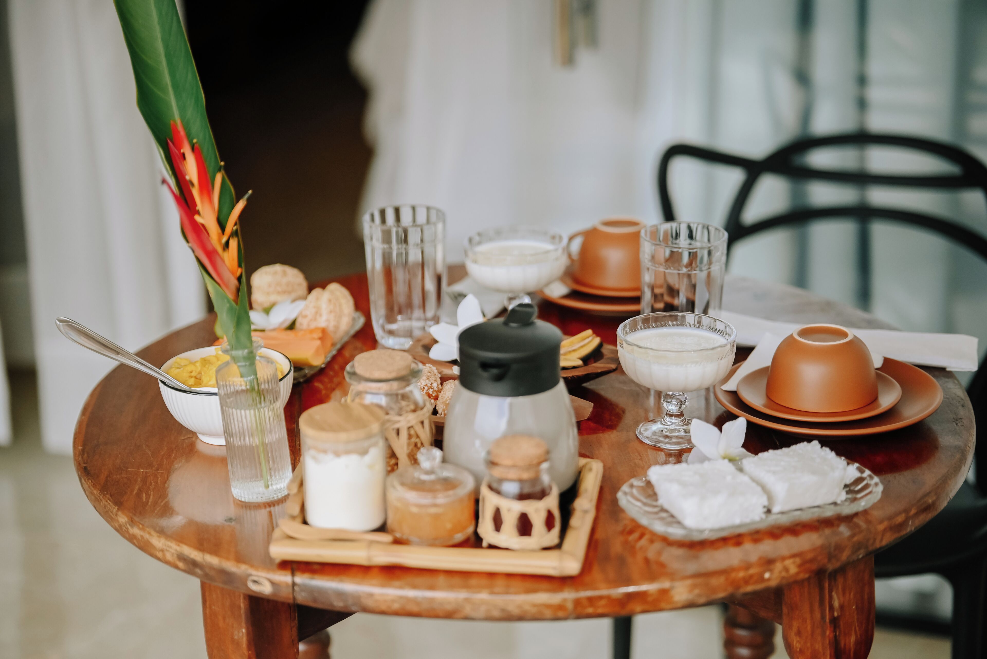 Una mesa de madera preparada con diversos productos para el desayuno, incluyendo un vaso de leche, una taza de té y un bol de fruta.