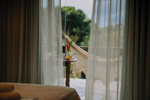 A room with a table and a view through sheer curtains to an outdoor area with greenery. - Pousada Almaré Boipeba (Cairu)