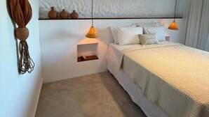 A modern bedroom with a bed, bedside lamps, a wall-mounted air conditioner, and a hanging decor piece. - Pousada Almaré Boipeba (Cairu)