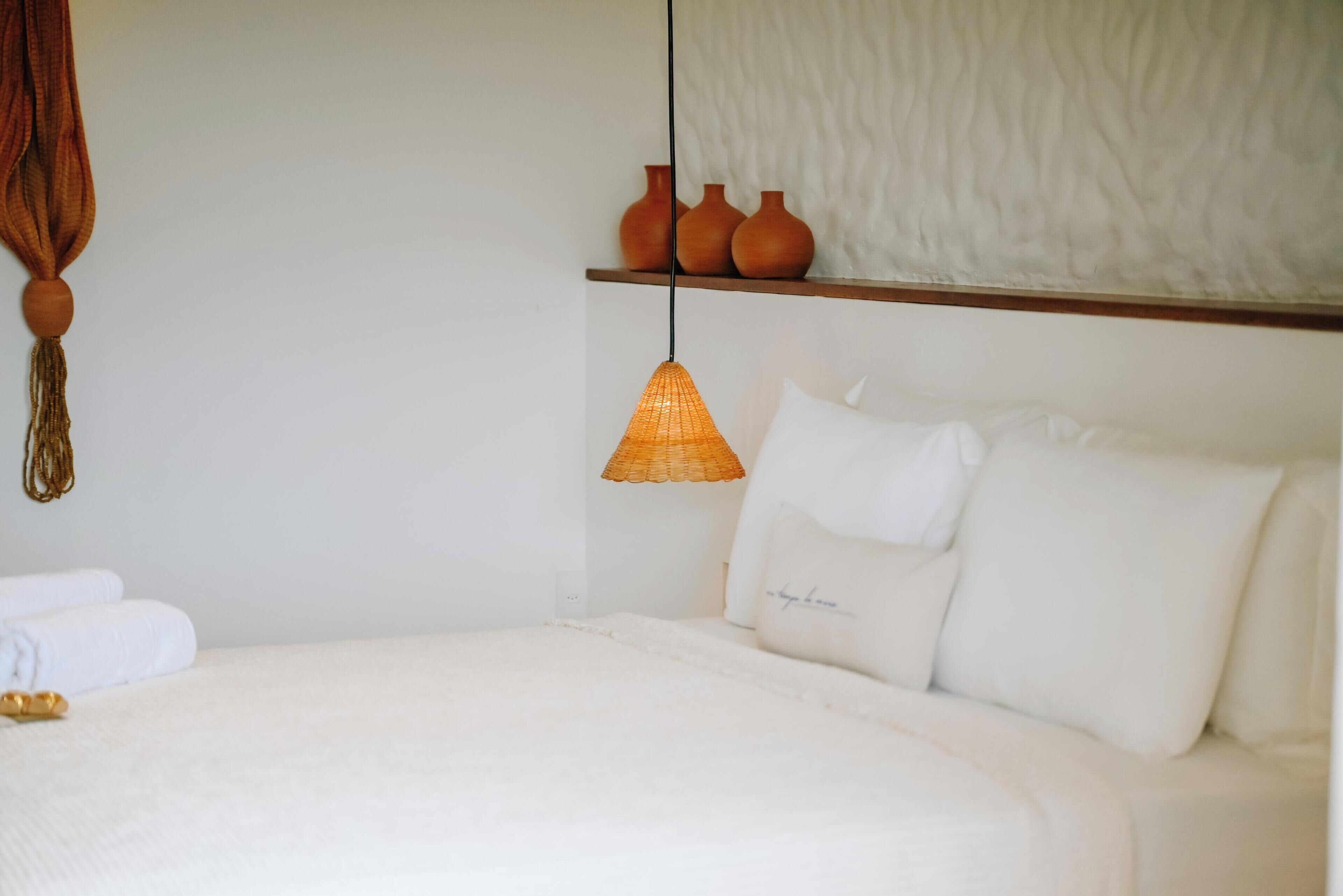 A bedroom with a bed, a hanging lamp, and a shelf with vases.
