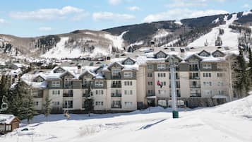 A snow-covered hotel with multiple floors, ski lift, and a mountainous backdrop.