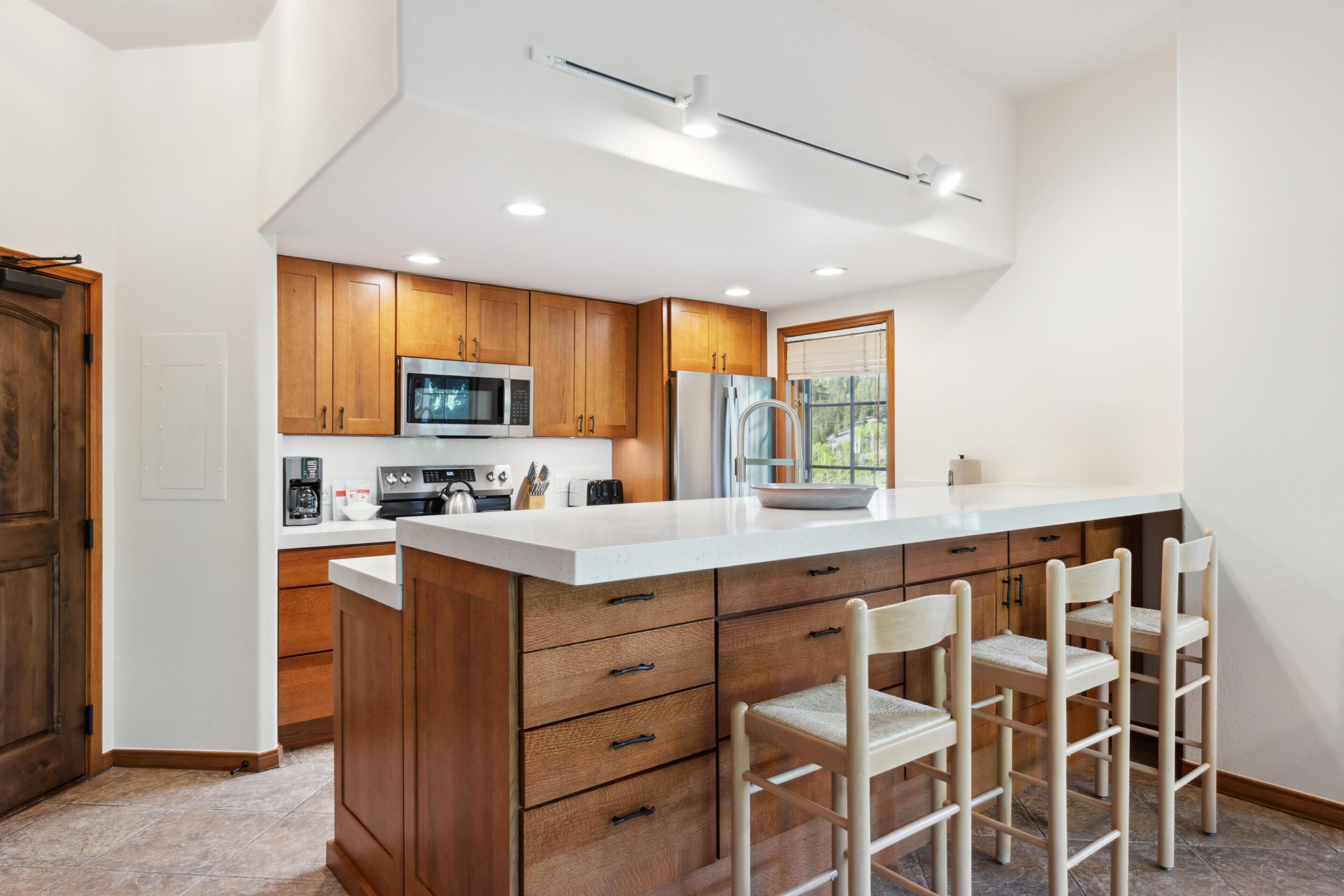 A modern kitchen with wooden cabinets, a white countertop, and a bar stool area.