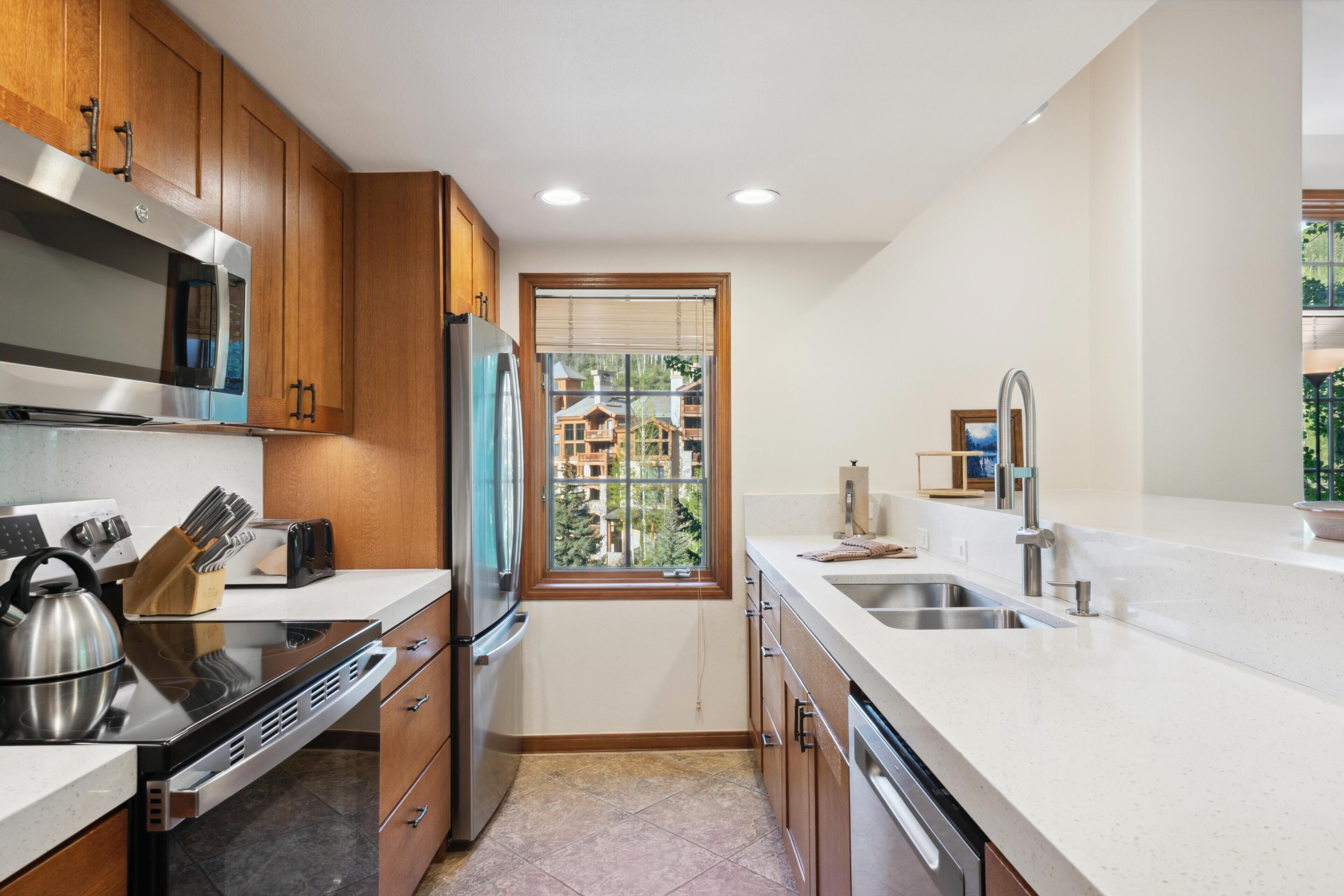 A modern kitchen with wooden cabinets, stainless steel appliances, and a window with a view of buildings.