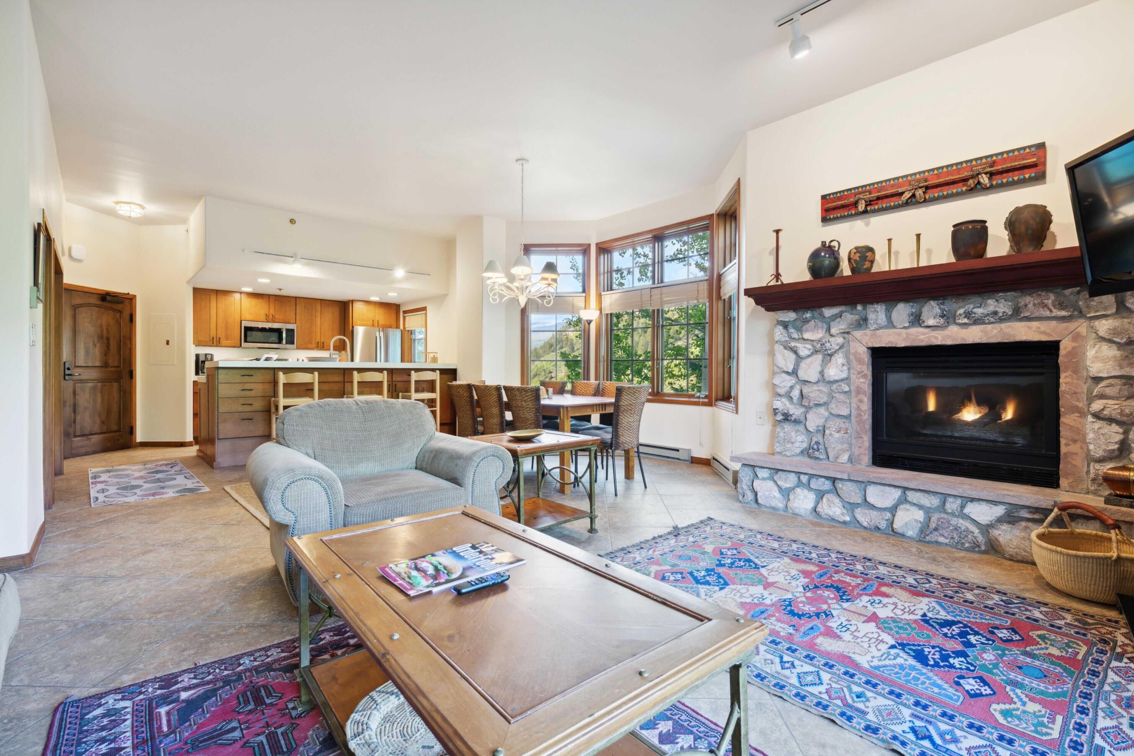 A spacious living area with a fireplace, a dining table, and a kitchen in the background.