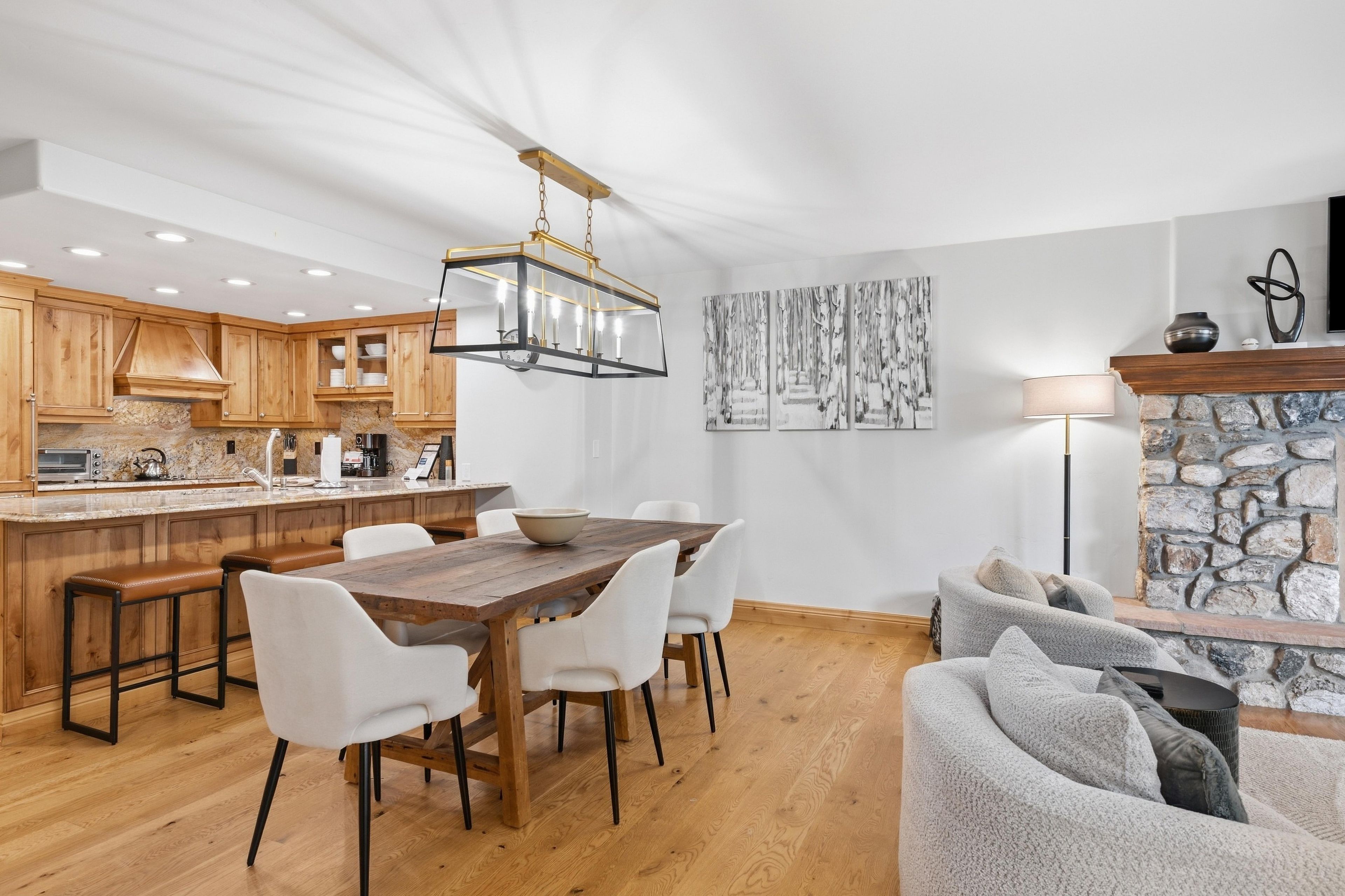 Una cocina moderna con armarios de madera, una isla central y una zona de comedor con una mesa de madera y sillas blancas.