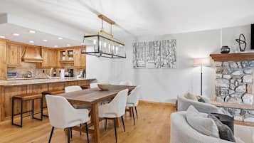 Una cocina moderna con armarios de madera, una isla central y una zona de comedor con una mesa de madera y sillas blancas.