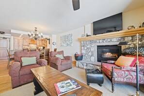 Una sala de estar con chimenea, televisor y comedor con armarios y sillas de madera.