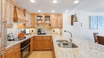 Una cocina con gabinetes de madera, encimeras de granito, pileta de acero inoxidable y una cafetera.