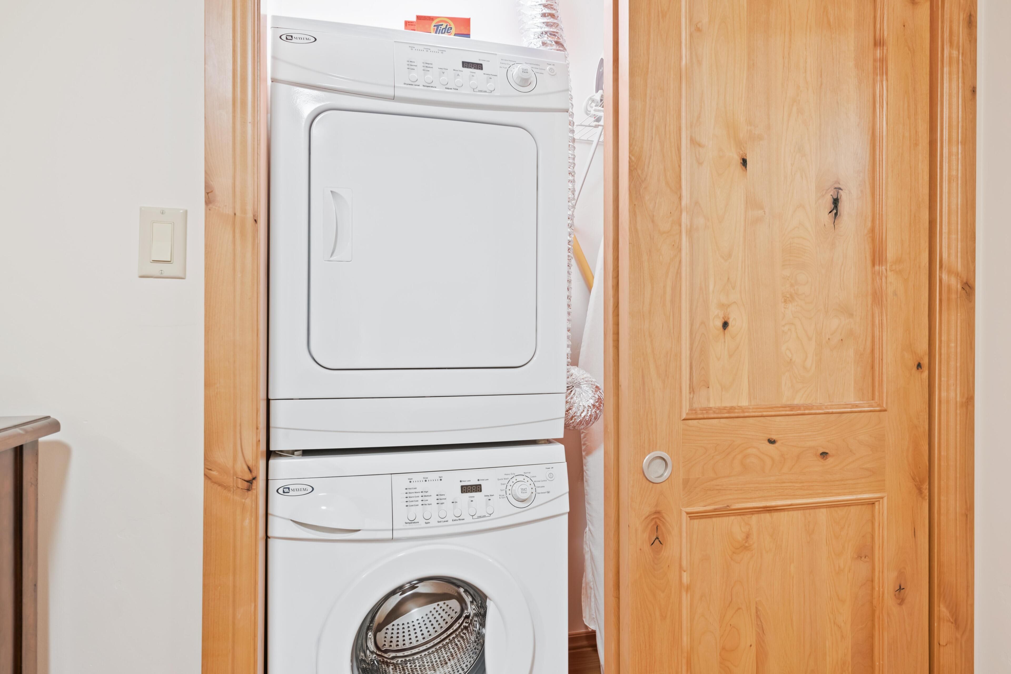 Lavadora y secadora apiladas en una habitación con una puerta de madera y un interruptor de luz en la pared.