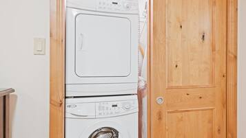 Lavadora y secadora apiladas en una habitación con una puerta de madera y un interruptor de luz en la pared.