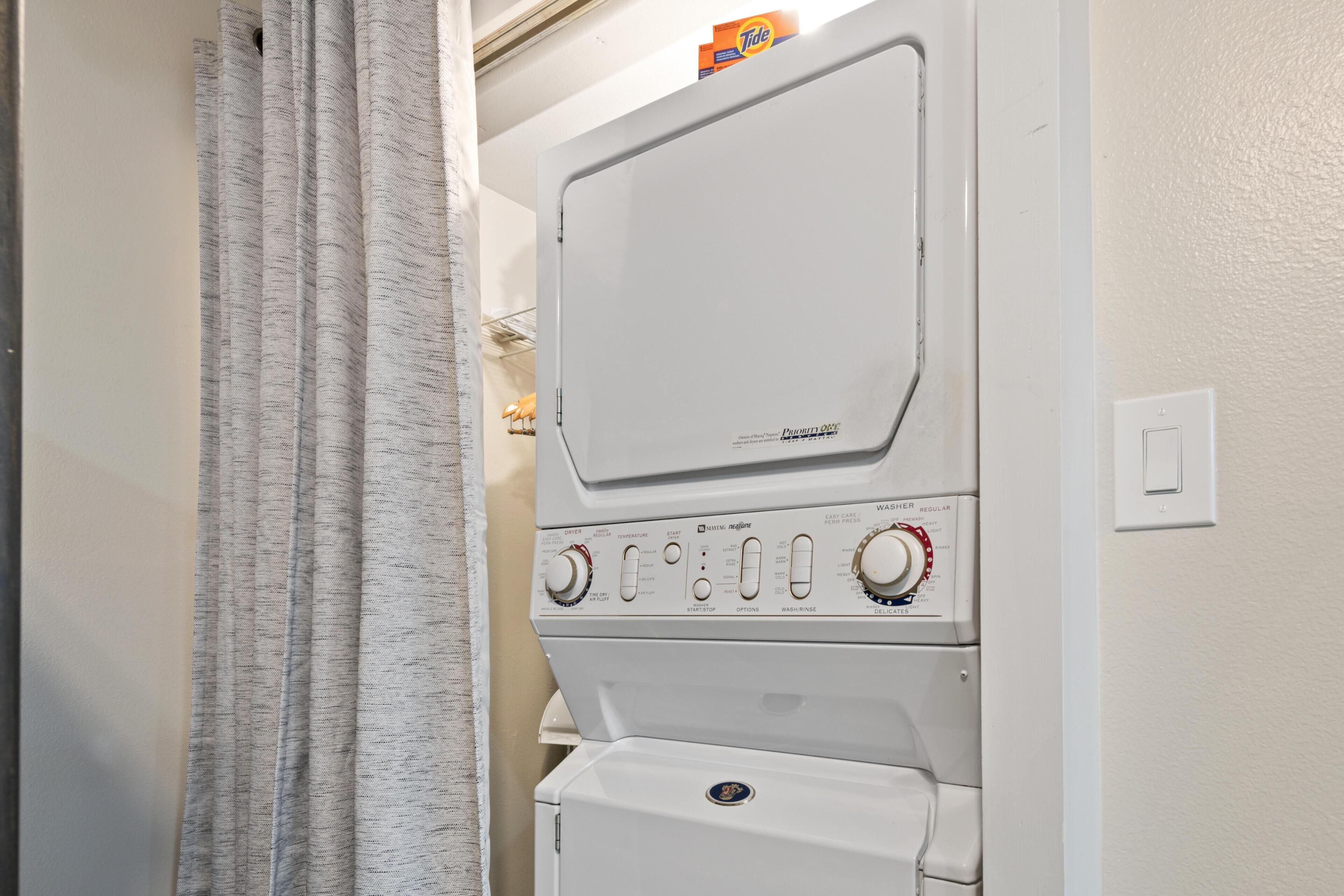 Een gestapelde wasmachine en droger met bedieningsknoppen en een doos wasmiddel van Tide bovenop.