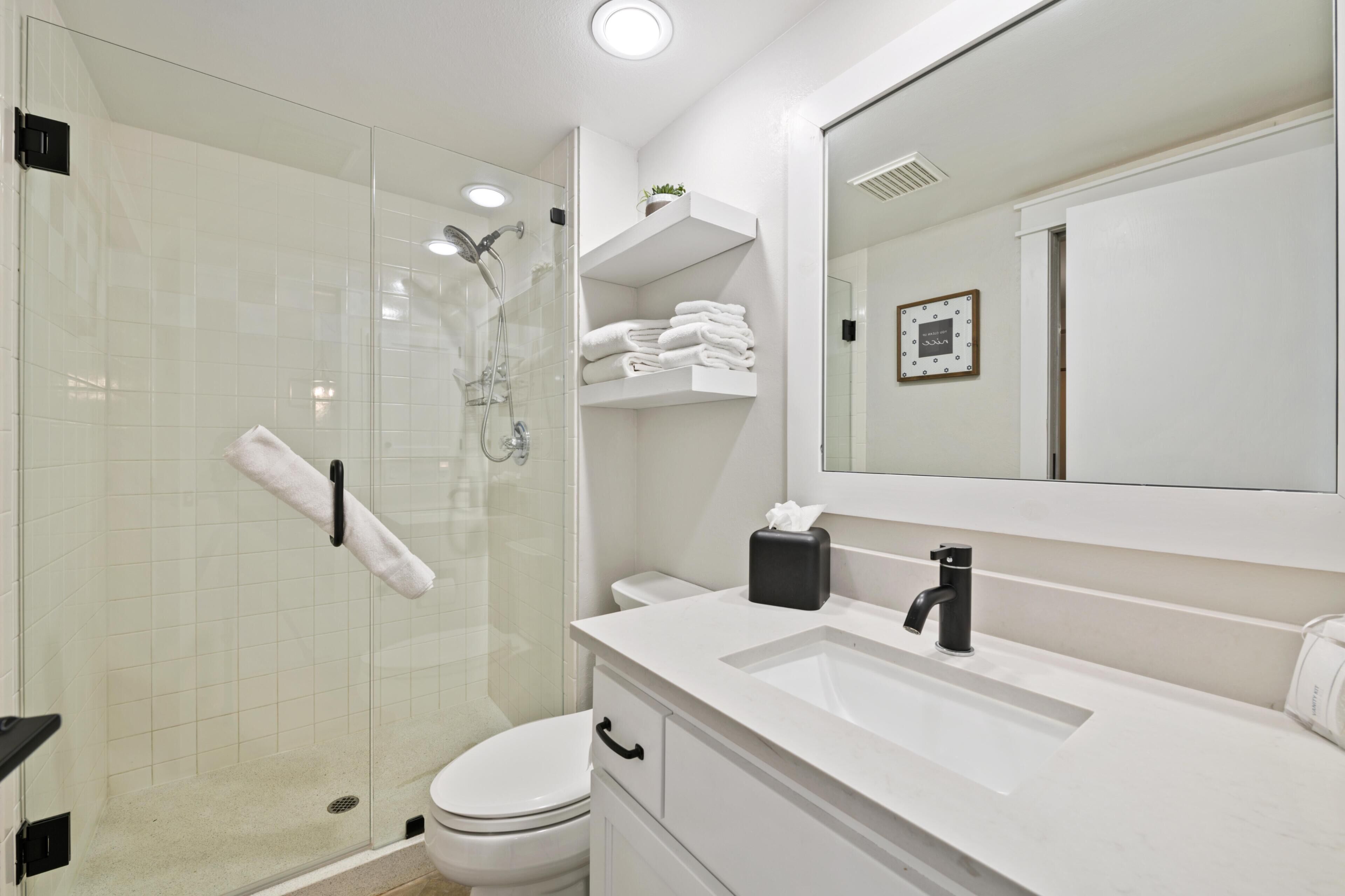A modern bathroom with a glass-enclosed shower, a white sink, and a large mirror.