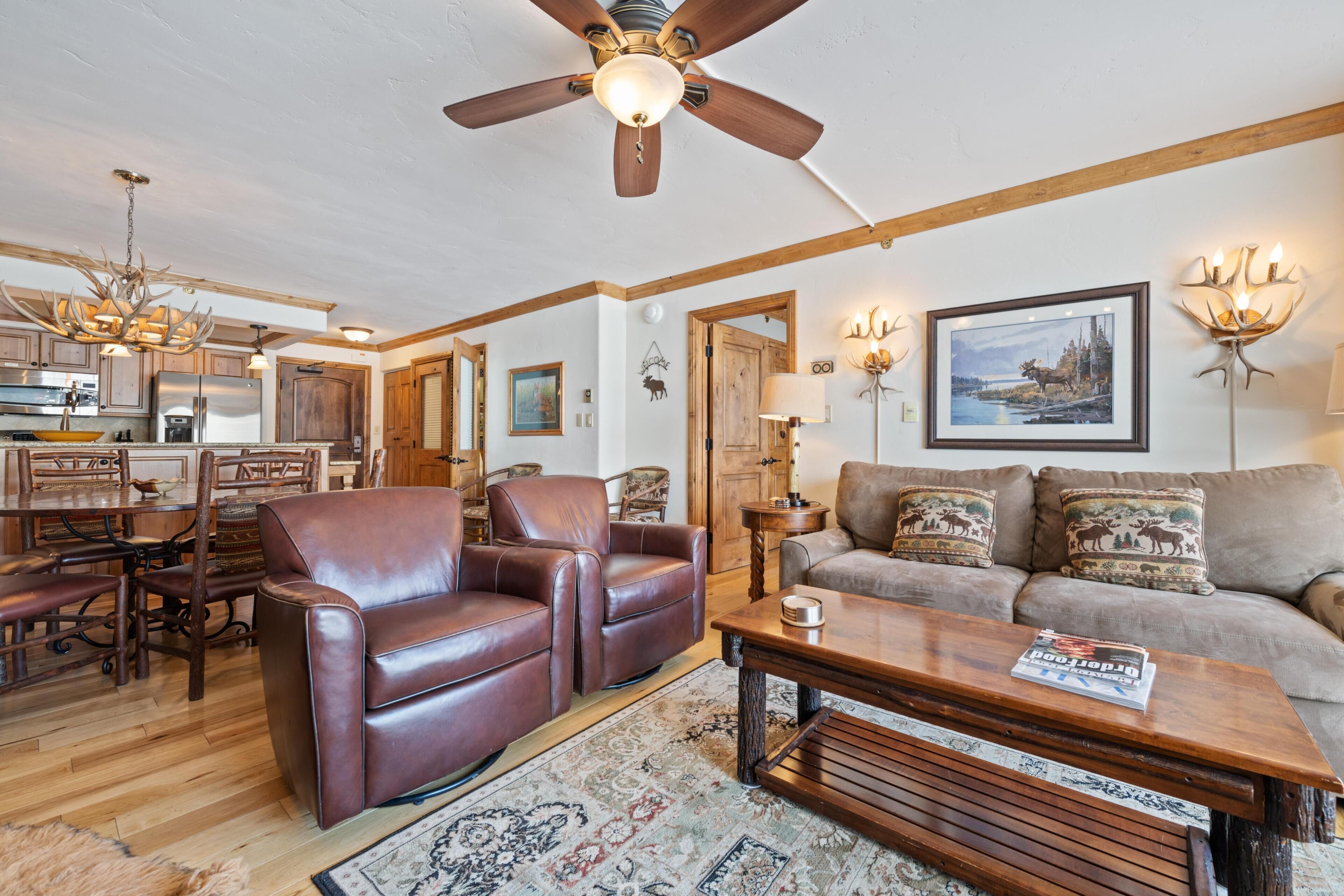 A spacious living room with a ceiling fan, a dining area with wooden chairs, a sofa with decorative pillows, and a coffee table.