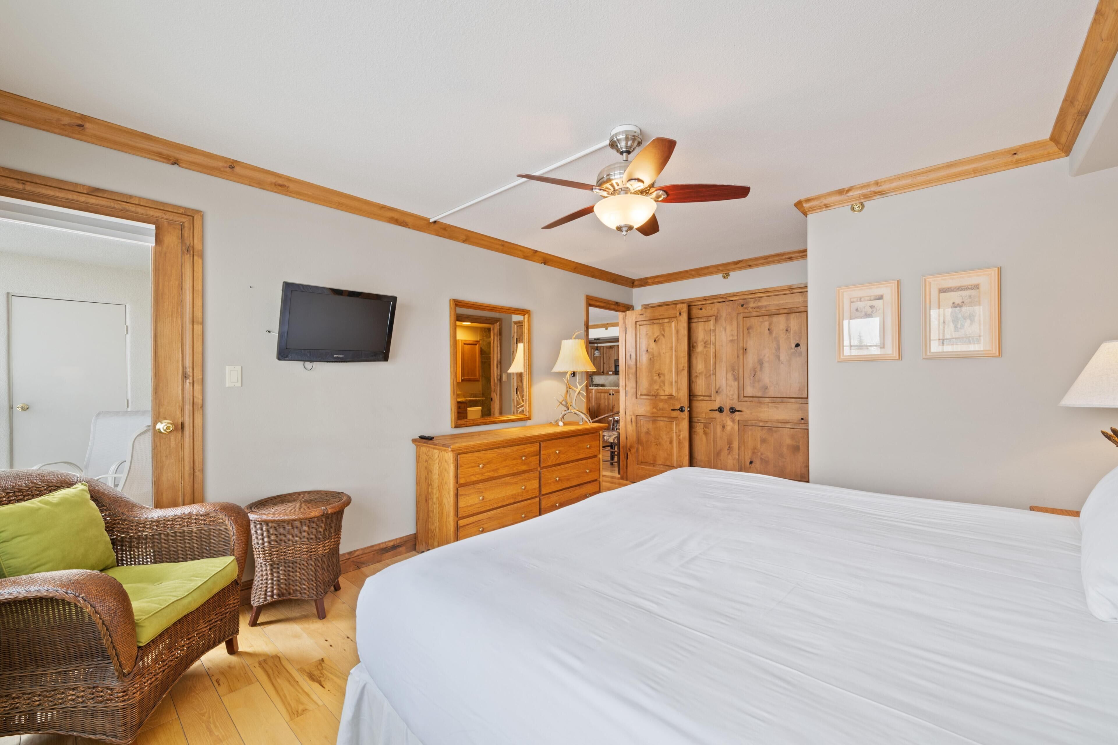 A bedroom with a bed, wooden wardrobe, a television, and a ceiling fan.