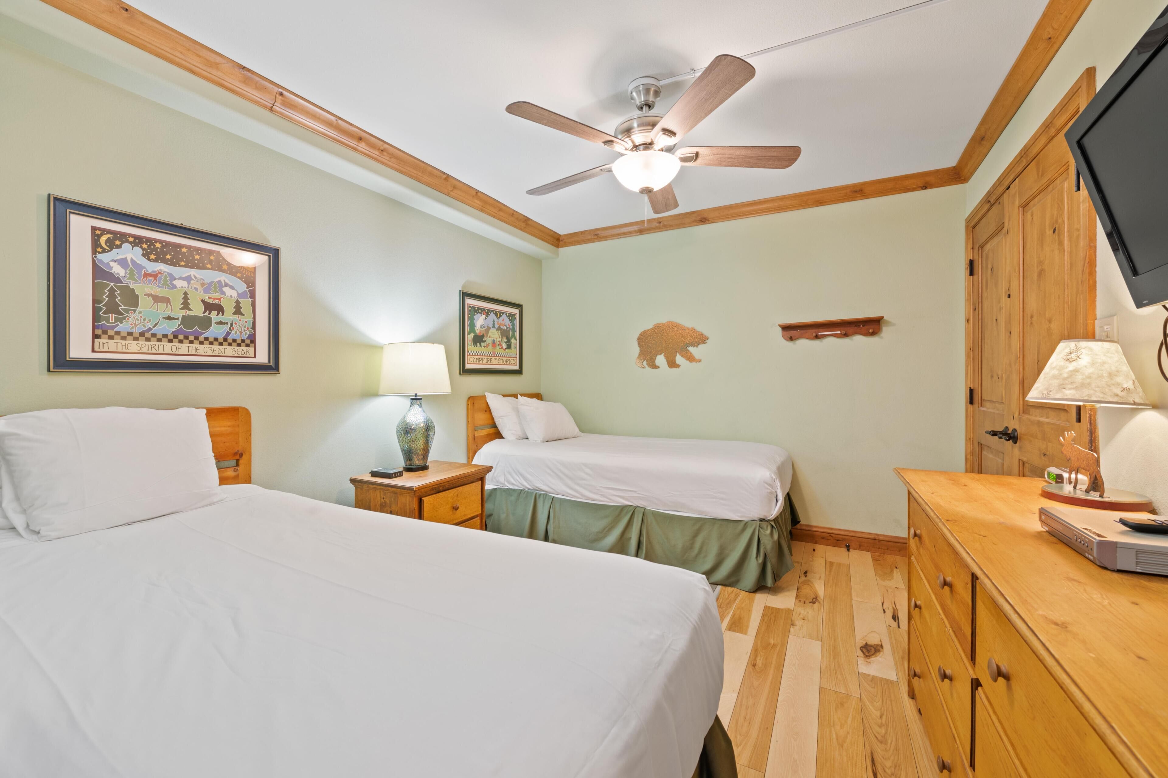 A bedroom with two beds, a ceiling fan, wooden furniture, and wall decorations.