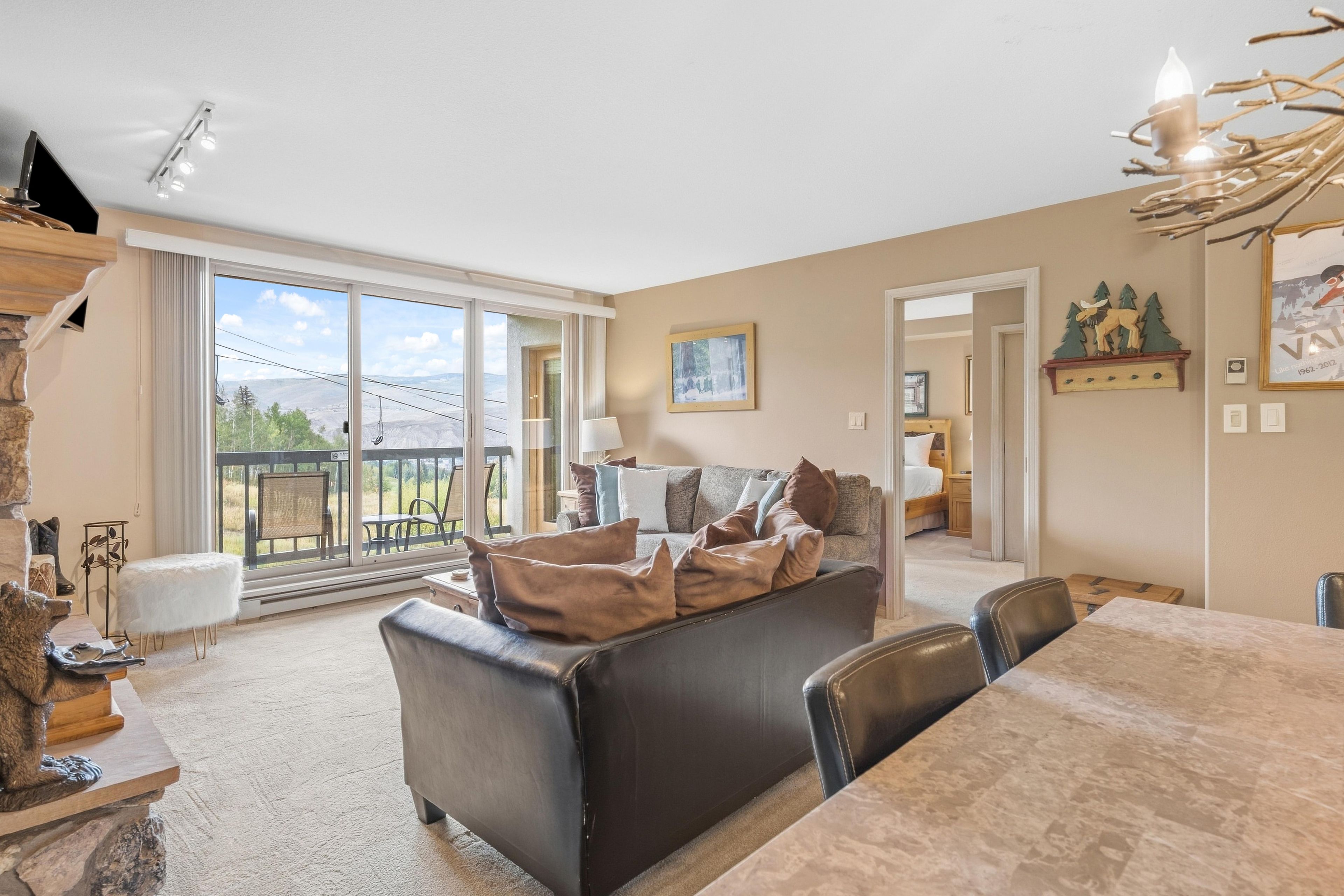 A spacious living room with a large sofa, a dining table, and a view through a sliding glass door to an outdoor area.