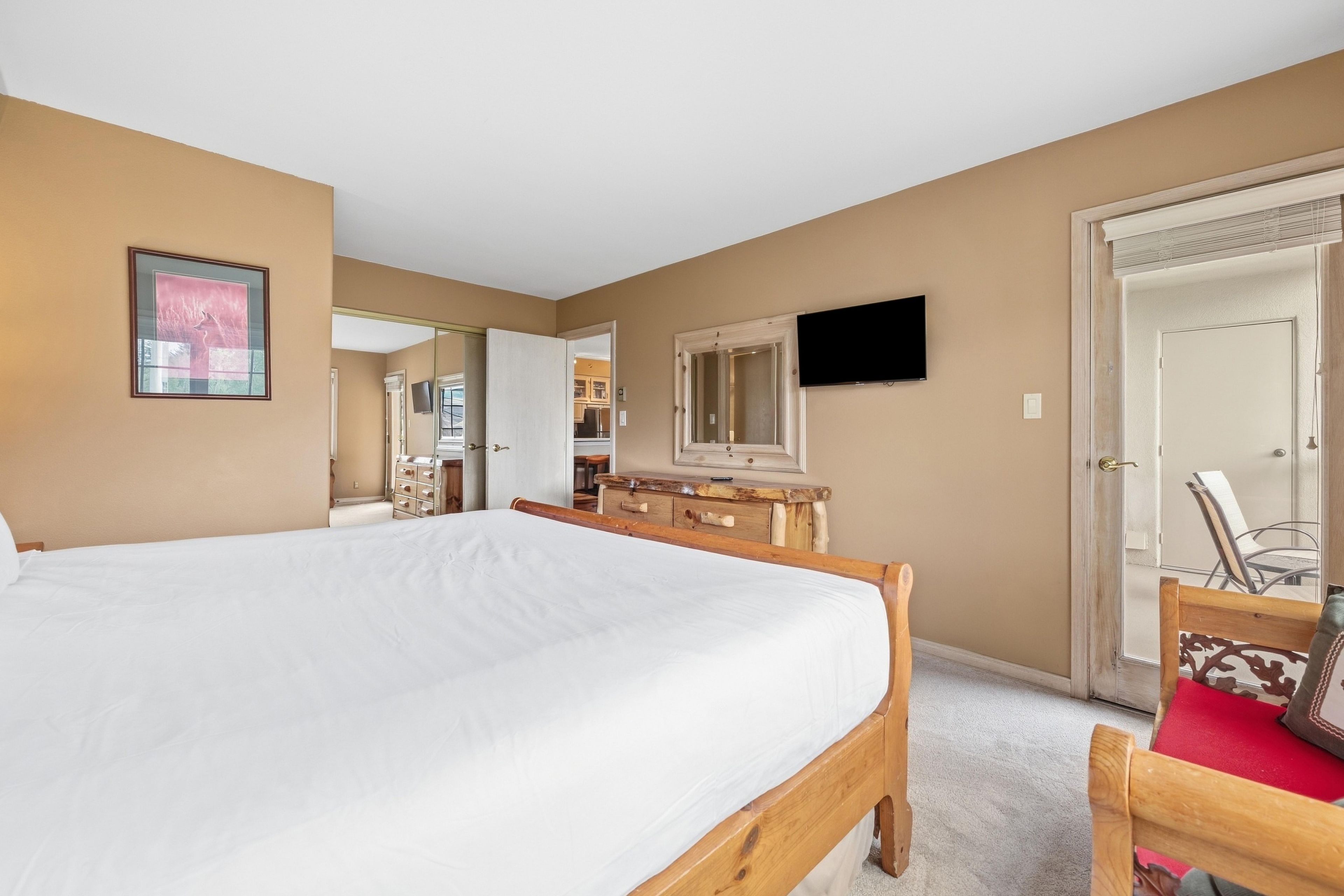 A hotel room with a large bed, a wooden dresser, a television, and a door leading to a bathroom.