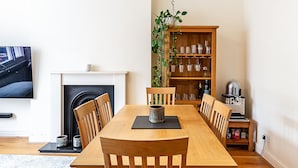 A dining room with a wooden table, chairs, a fireplace, a bookshelf, and a television. - Traditional Earl’s Court Apartment (London)