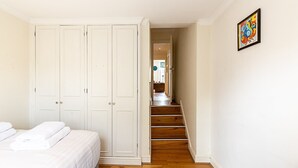 A bedroom with a bed, a wardrobe, a staircase leading to a hallway, and a painting on the wall. - Traditional Earl’s Court Apartment (London)