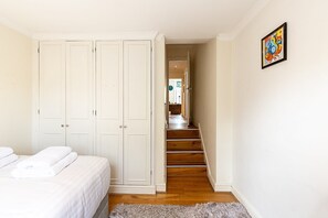 Ein Schlafzimmer mit Bett, Kleiderschrank, einer Treppe zu einem Flur und einem Bild an der Wand.