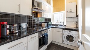 A modern kitchen with a gas stove, coffee maker, toaster, and washing machine. - Traditional Earl’s Court Apartment (London)