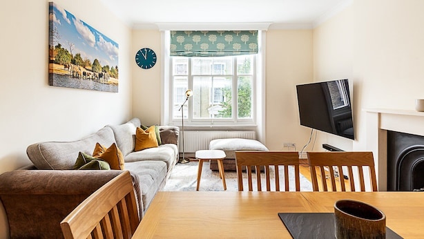 A living room with a sofa, a dining table, chairs, a TV, and a fireplace. - Traditional Earl’s Court Apartment (London)