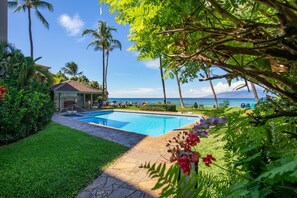 Ein Swimmingpool mit Liegestühlen, Palmen und Blick aufs Meer.