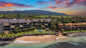 Ein Resort mit mehreren Gebäuden, einem Schwimmbad, einem Strand und Bergen im Hintergrund.