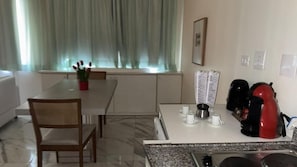 Eine moderne Küche mit Esstisch, Stühlen, einer Kaffeemaschine und einem Fenster mit Vorhängen.