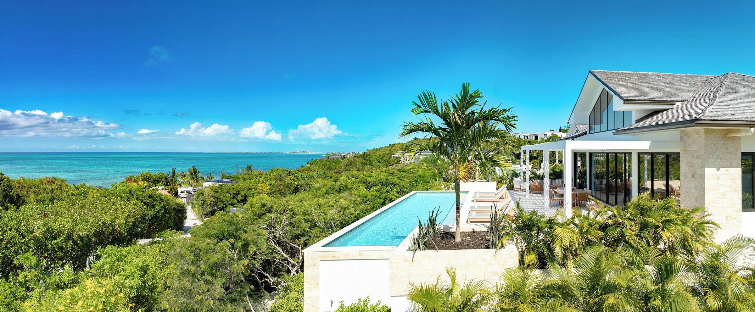 Una casa moderna con piscina, rodeada de exuberante vegetación y con vistas al mar azul cristalino.