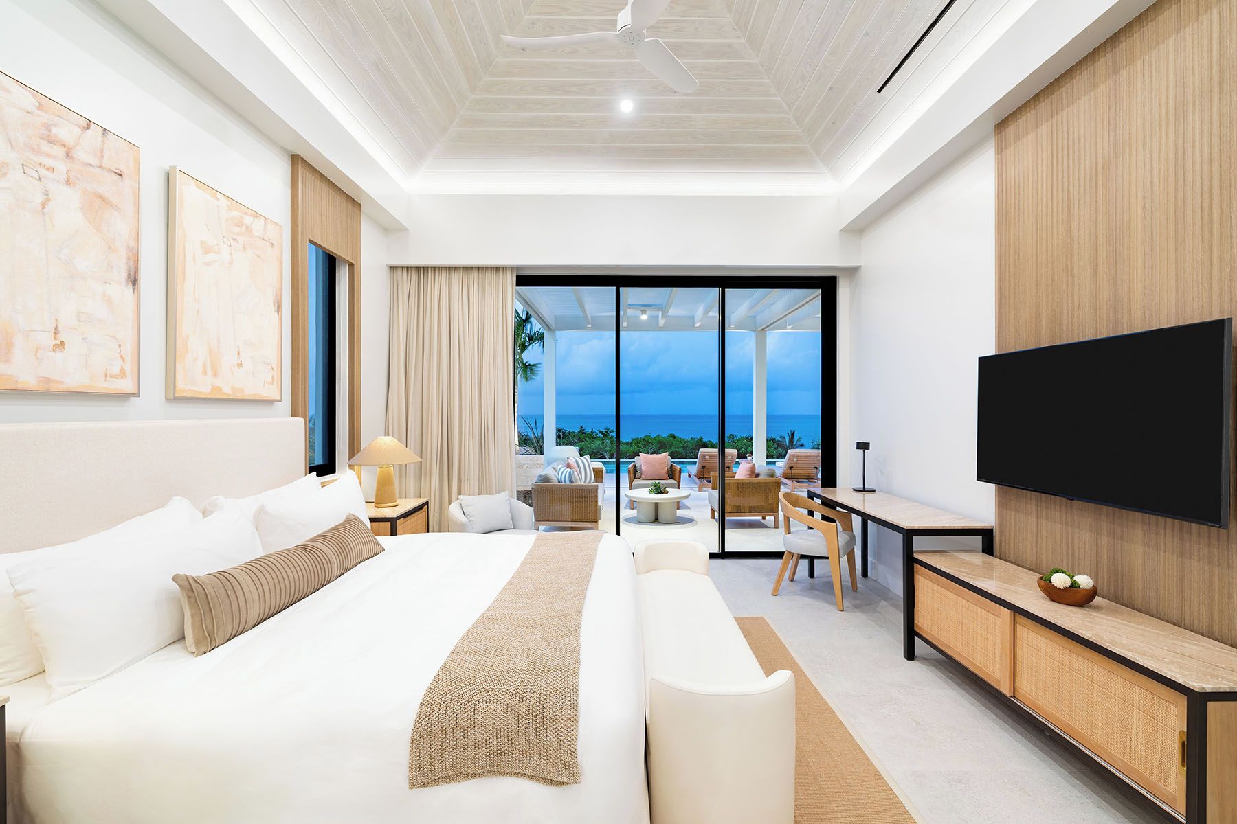 Una habitación de hotel moderna con una cama grande, un escritorio, un televisor de pantalla plana y un balcón con vistas al océano.