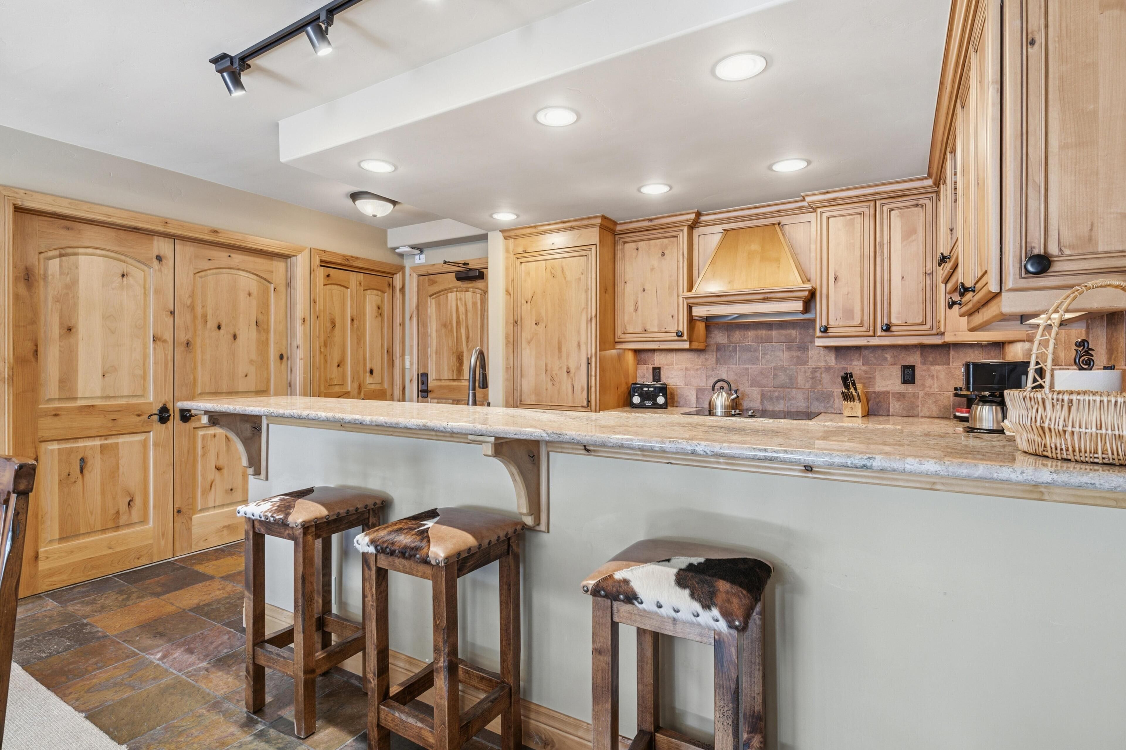 A kitchen with wooden cabinets, a stone backsplash, and a bar area with stools.