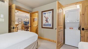 A bedroom with a bed, a washing machine, wooden doors, a poster, and a dining area.
