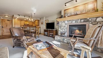 Una sala de estar con chimenea de piedra, sillones de cuero, una mesa de centro de madera y un televisor.